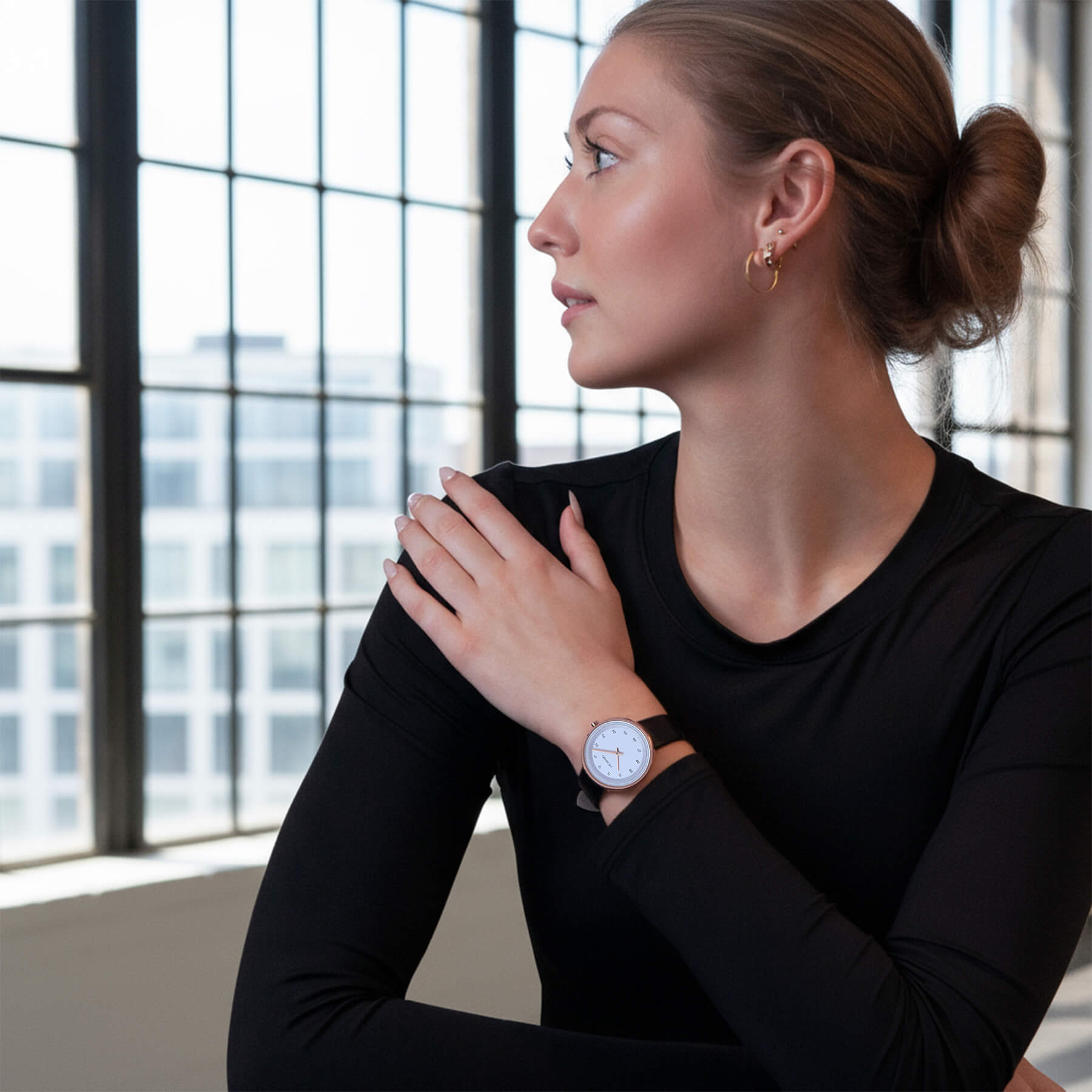 white VEJRHØJ  ladies watch. Woman wearing a black top and a petite arctic watch, sitting indoors with large windows in the background