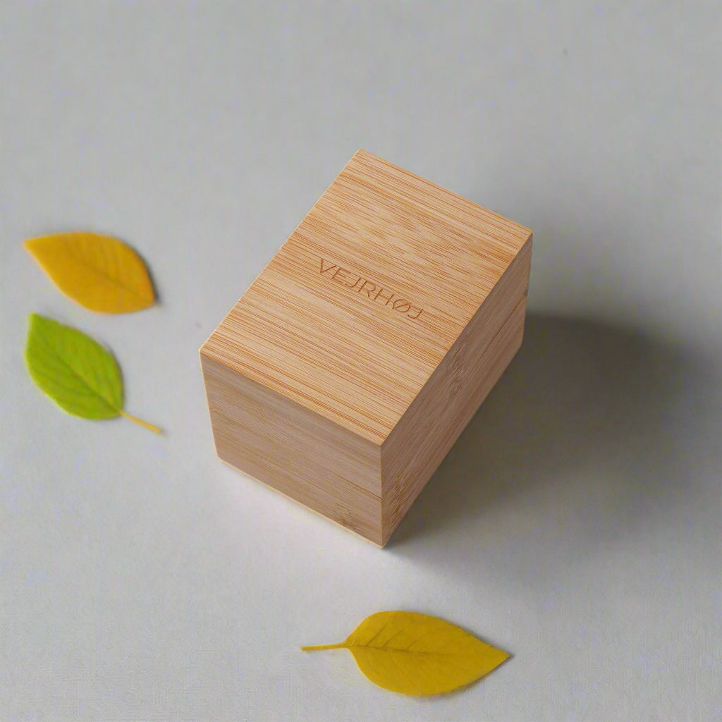 Wooden box with 'VEJRHØJ' branding on a light background with leaves.