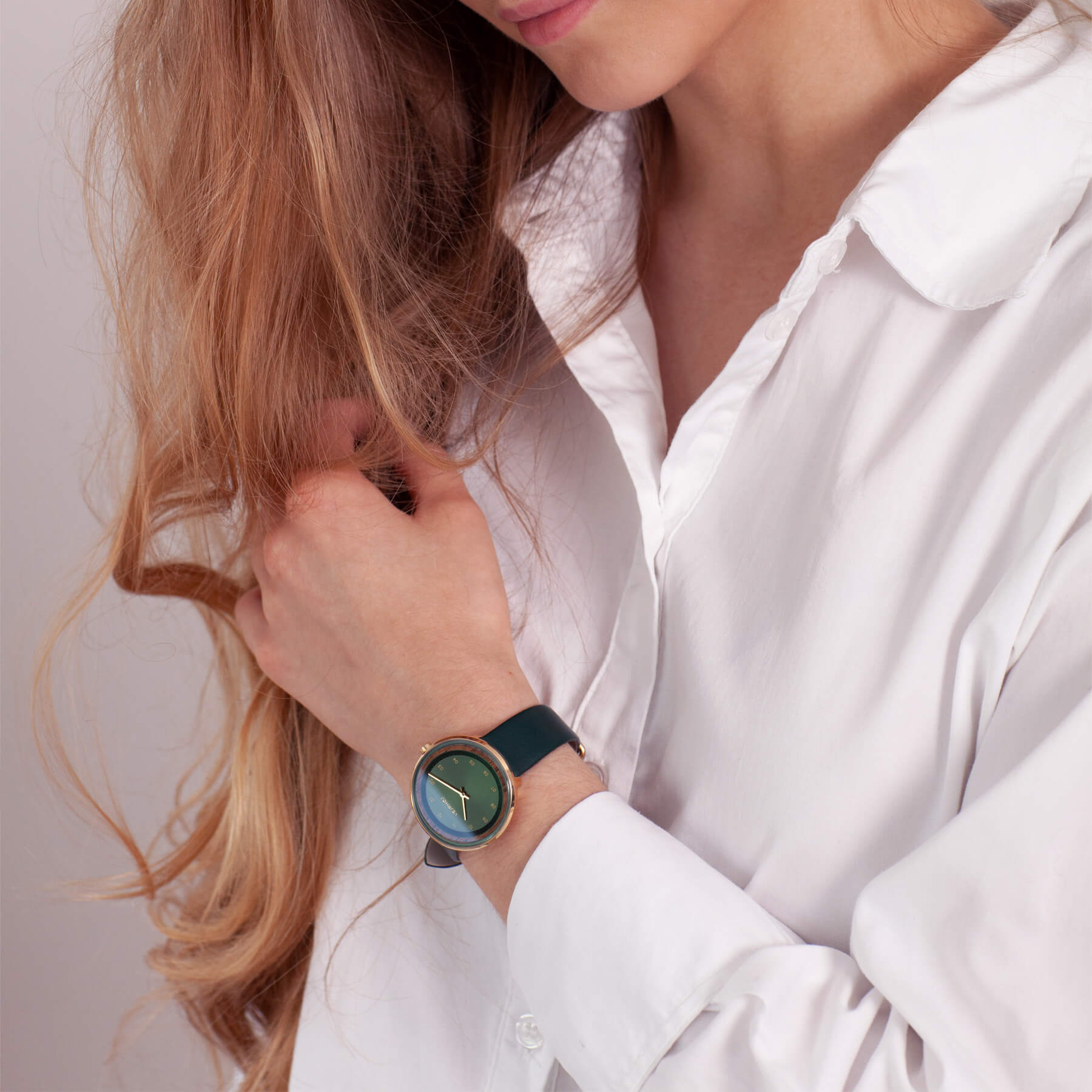 women long hair and a white shirt wearing a green and golden watch