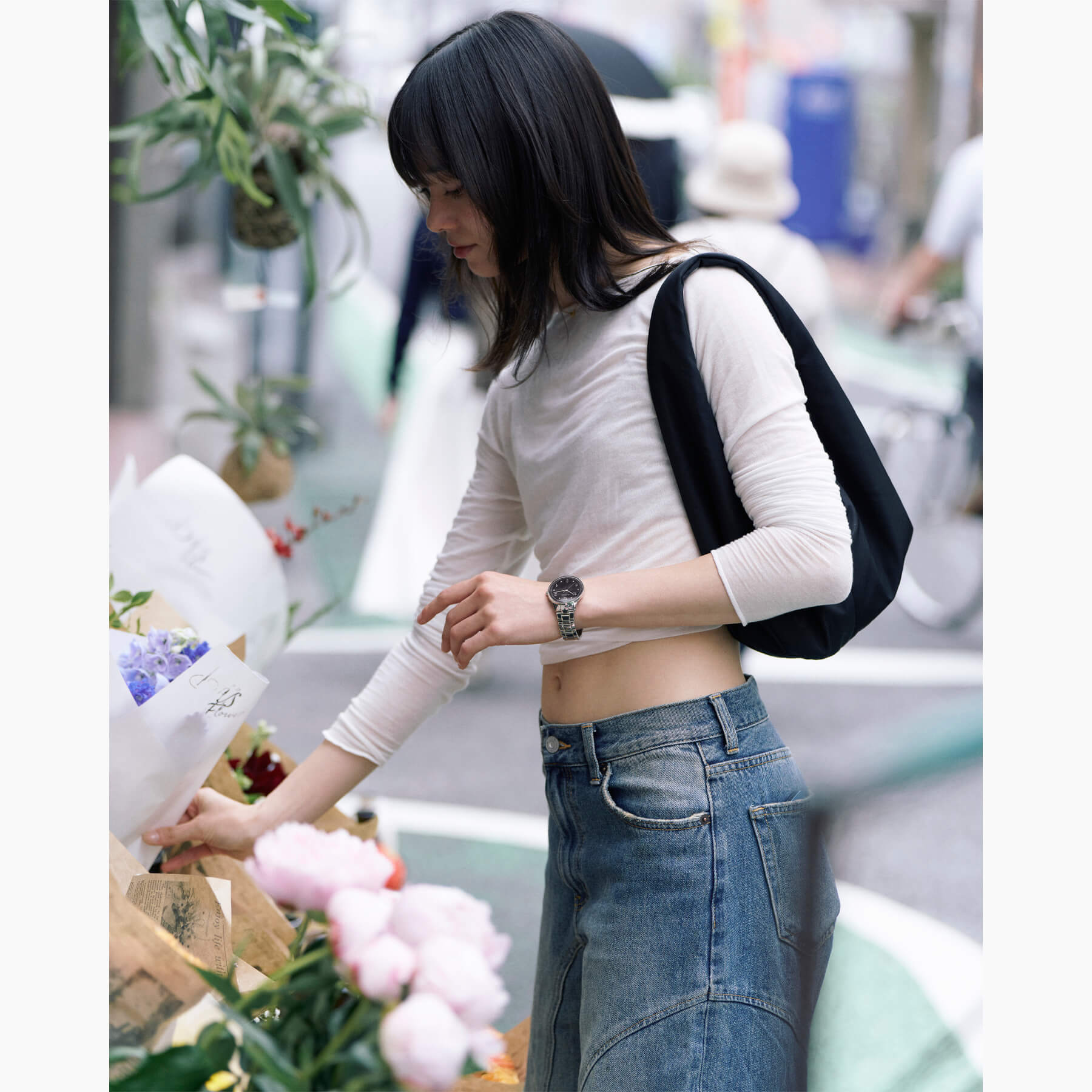 Woman wearing Vejrhøj Petite Royal Black, scene of choosing a bouquet at a florist. Scandinavian design watch with black wood grain dial and silver bracelet shines in natural light.