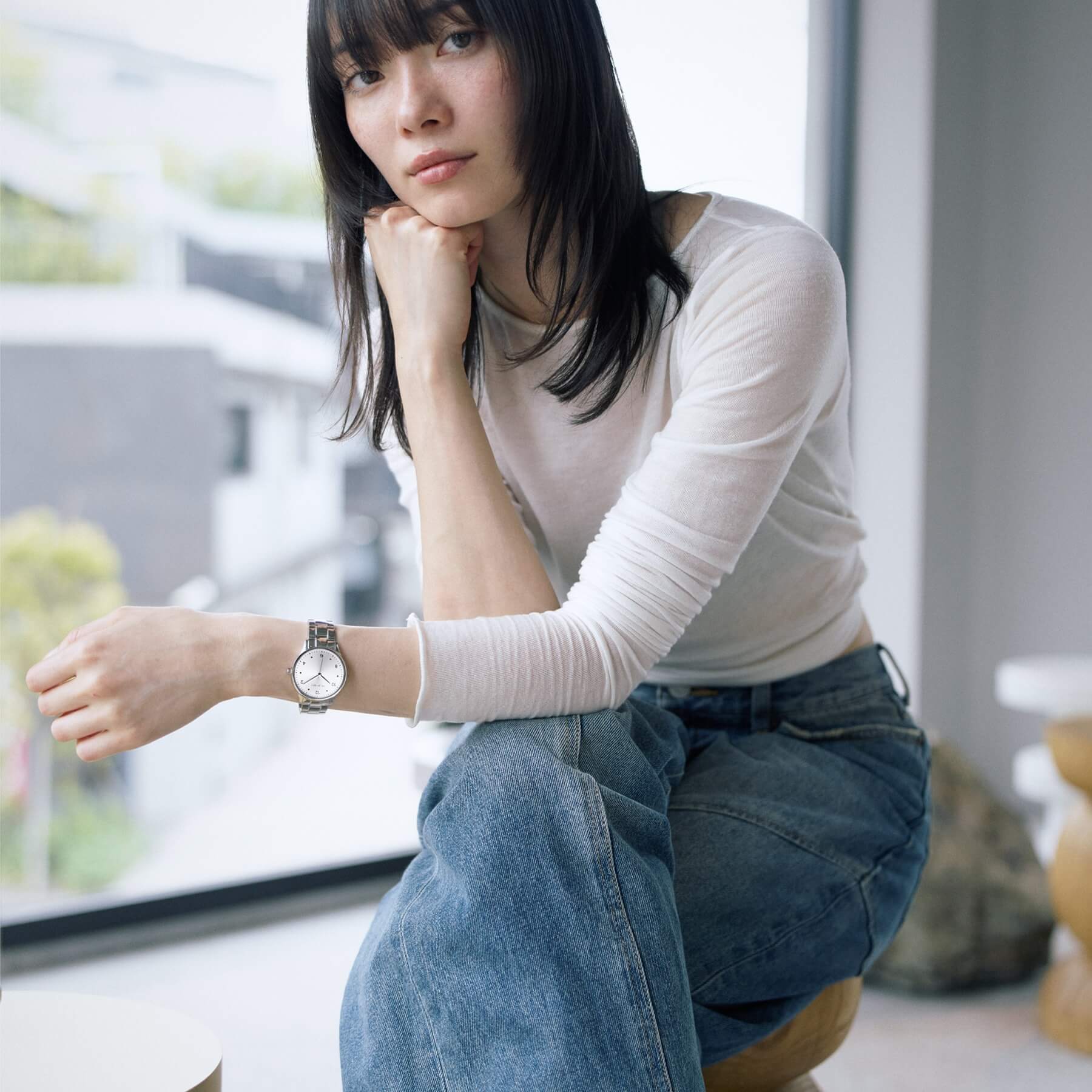 Woman wearing VEJRHØJ Petite Royal Silver, Scandinavian design watch with sunray silver dial and stainless steel belt with white top and denim